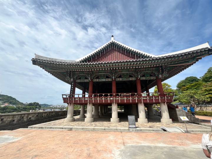 Traditional Korean wooden pavilion with ornate roof and elevated platform under a bright sky.