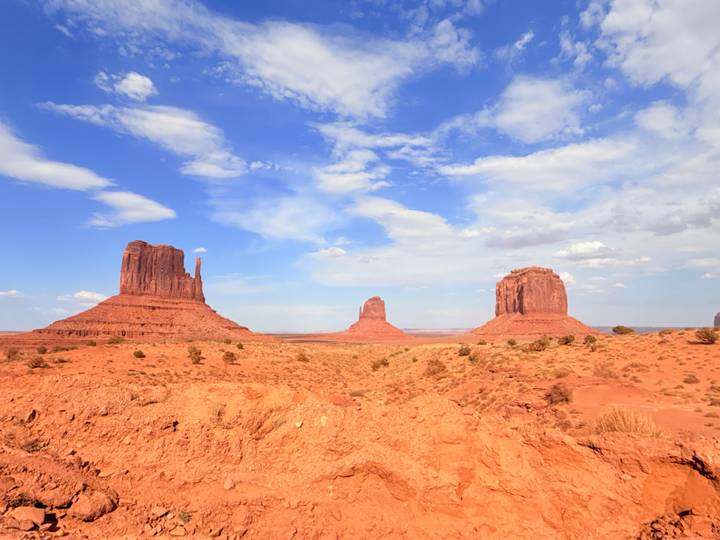 Iconic Mittens of Monument Valley rising from a red desert under bright blue sky
