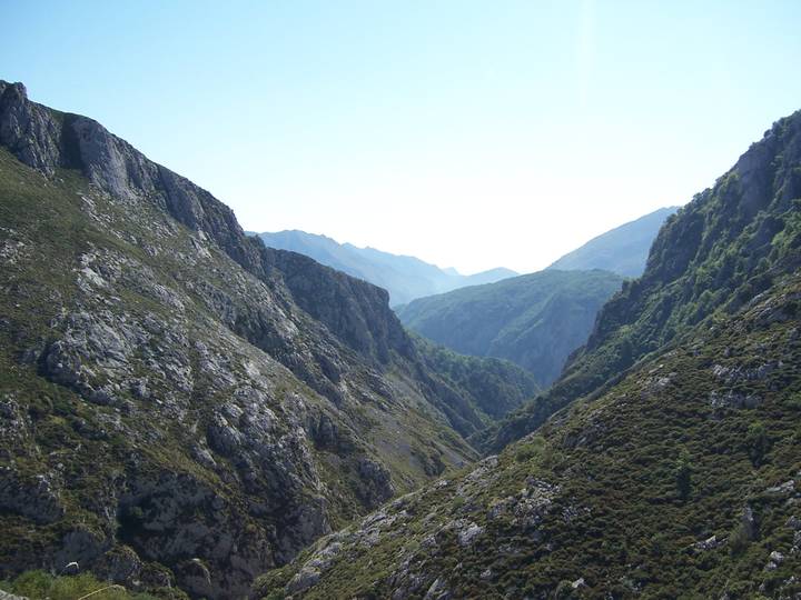 Wide rocky gorge framed by steep, rugged mountains under a clear blue sky.