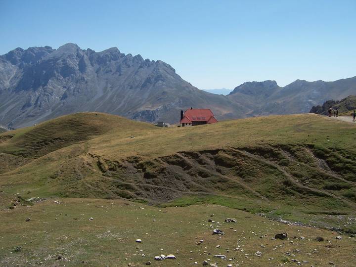 Alpine meadow with a lone red-roofed hut set against jagged grey peaks.