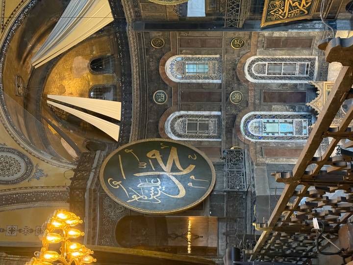 Interior gallery of Hagia Sophia showing giant Arabic calligraphy medallion and ornate mosaics.