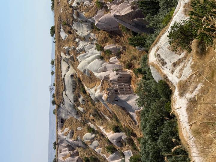 Eroded tuff hills and cave dwellings of Cappadocia rise among pale rock formations under clear sky.