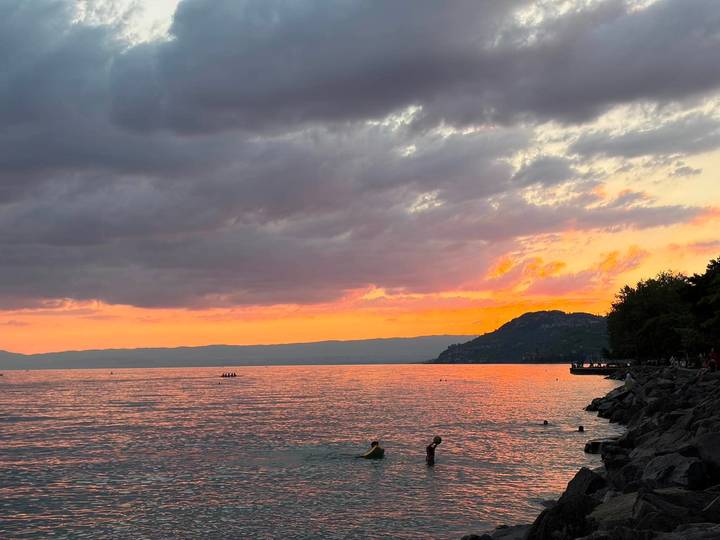 Pink and orange sunset colours reflect on the calm waters of Lake Geneva as swimmers enjoy the evening.