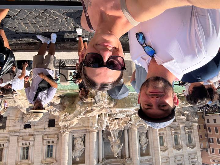 Couple takes a selfie at the Trevi Fountain surrounded by other tourists in Rome.