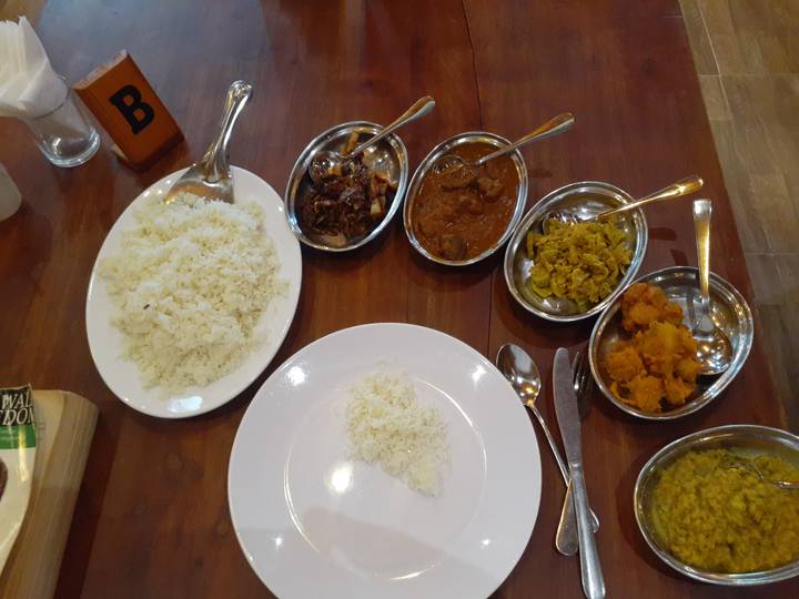 Sri Lankan meal with a plate of white rice and several small metal dishes filled with various curries laid out on a wooden table.