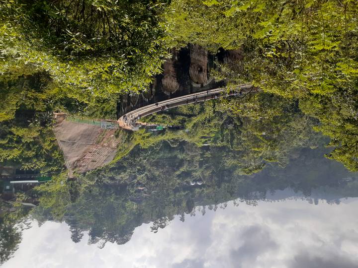 Lush green valley view of Sri Lanka’s Nine Arch Bridge curving across a ravine with small figures walking along its span.