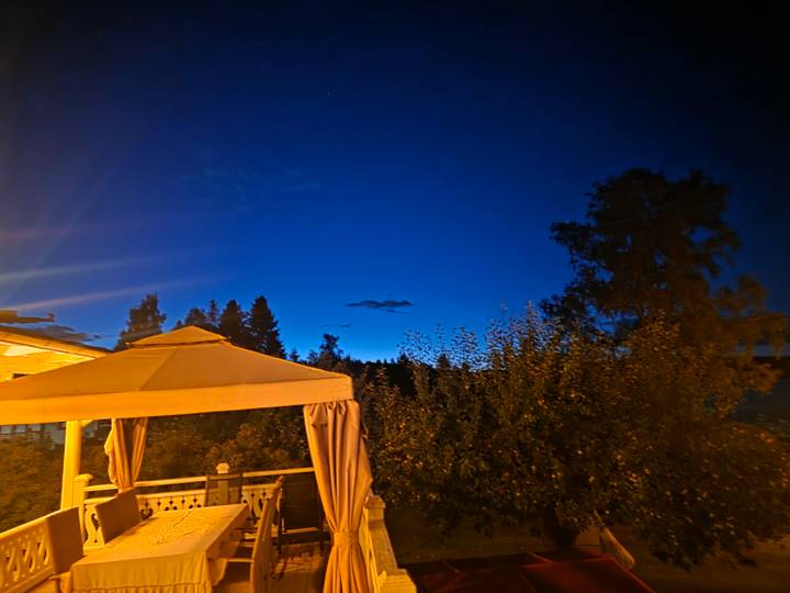 Deep blue twilight sky above lit gazebo and treetops after sunset.