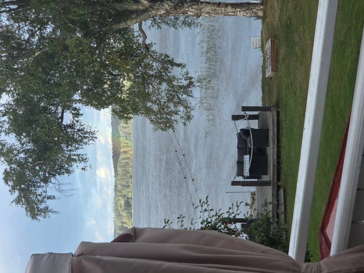 Lakeside patio with sofa overlooking wide water and forested opposite shore.
