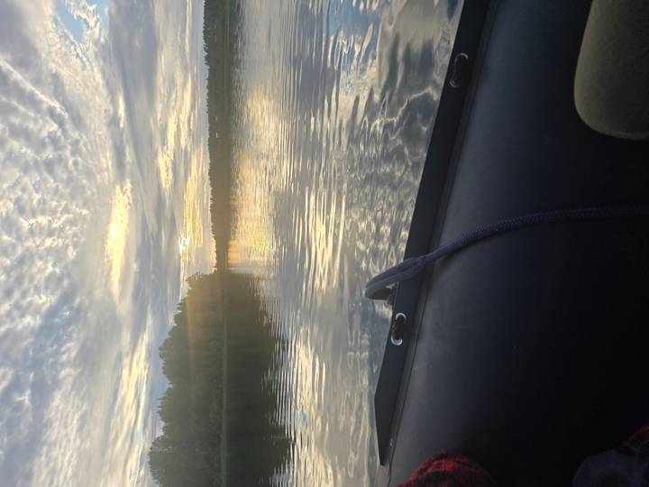 Tranquil lake at sunset viewed from boat with rippled water reflecting golden sky.