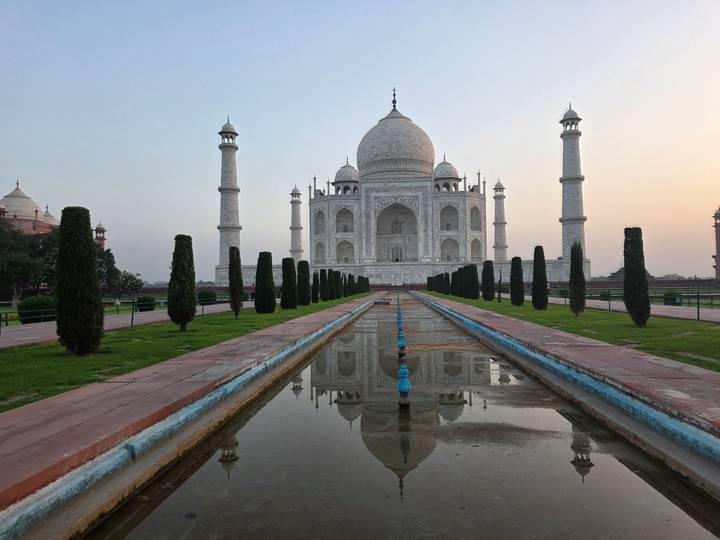 Symmetric view of Taj Mahal at dawn reflected in long water channel.