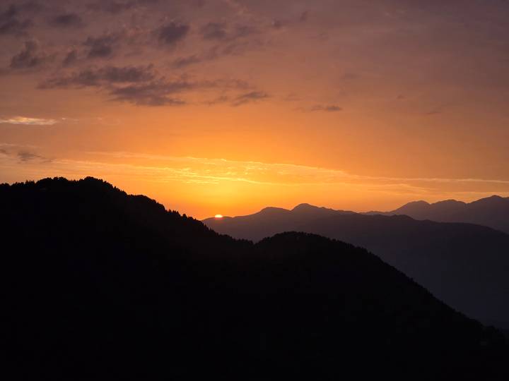 Fiery orange sunset dipping behind layered mountain silhouettes.