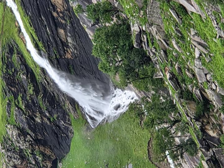 Tall waterfall cascading down rocky green mountainside.