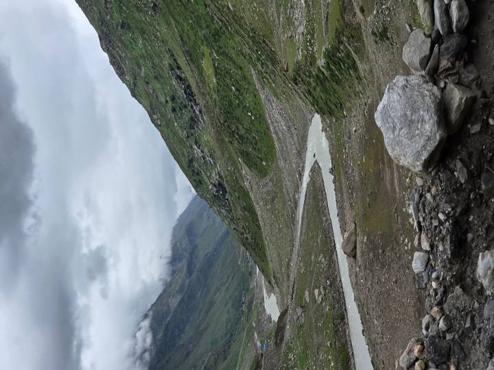 Winding river flowing through rocky alpine valley under cloudy skies.