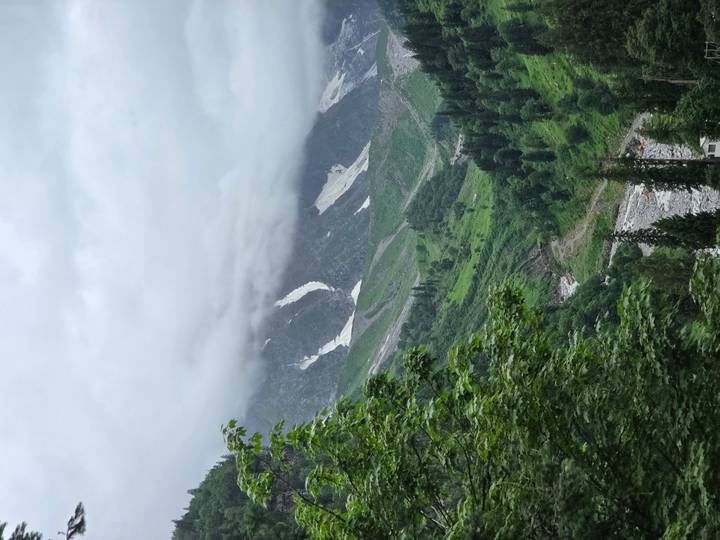 Lush green valley with patches of lingering snow beneath cloud-shrouded peaks.