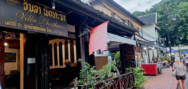 Charming street scene with traditional Lao guesthouses, a pink flag, and evening pedestrians.