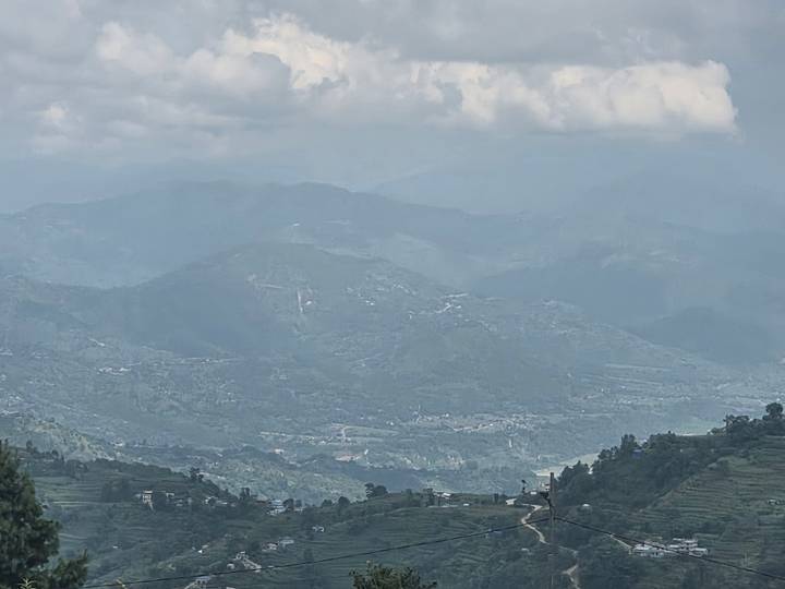 Hazy view across terraced hills and distant mountain ridges beneath a cloudy sky.