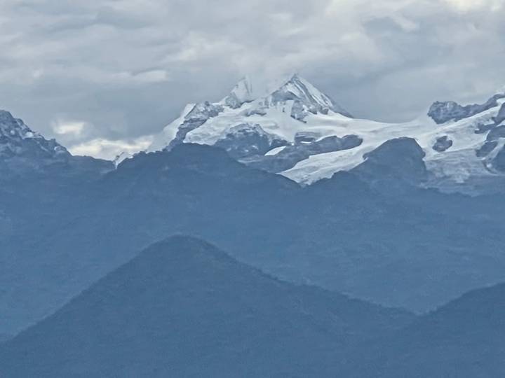 Snow-capped Himalayan peak rising above lower dark ridges on a cloudy day.