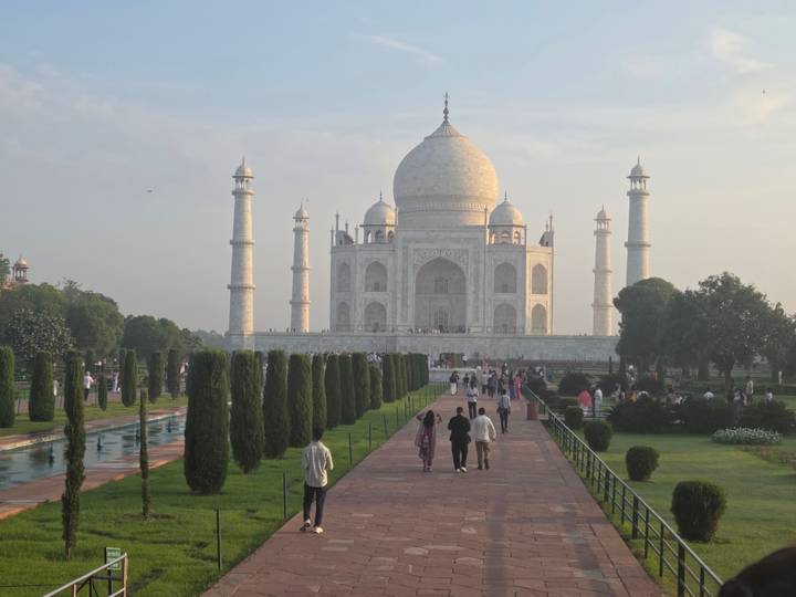 Iconic frontal view of the Taj Mahal with visitors strolling along the long reflecting pool at golden hour.