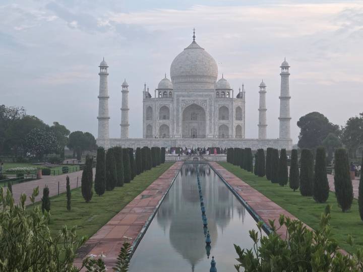 Early morning view of the Taj Mahal mirrored in the central water channel with visitors gathered near the entrance.