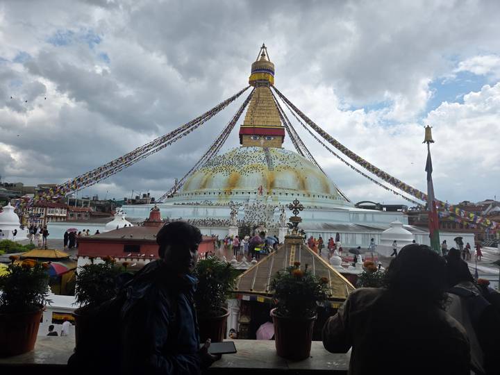 Boudhanath Stupa with colorful prayer flags and crowds of pilgrims beneath dramatic clouds.