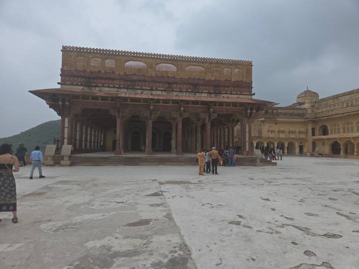 Visitors explore a vast marble courtyard inside Amber Fort under a grey sky.