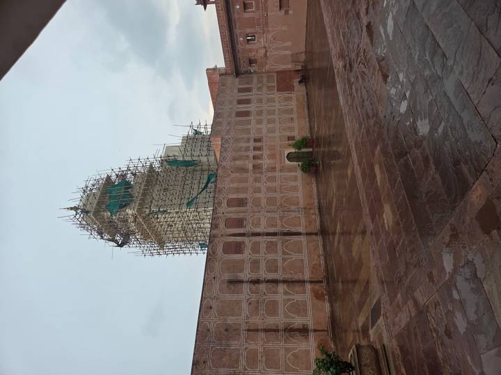 Courtyard of an Indian palace or mosque with a tall tower covered in scaffolding on a rainy day