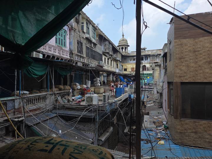 Narrow alley filled with tangled electrical wires, small shops, and several locals in an old market area