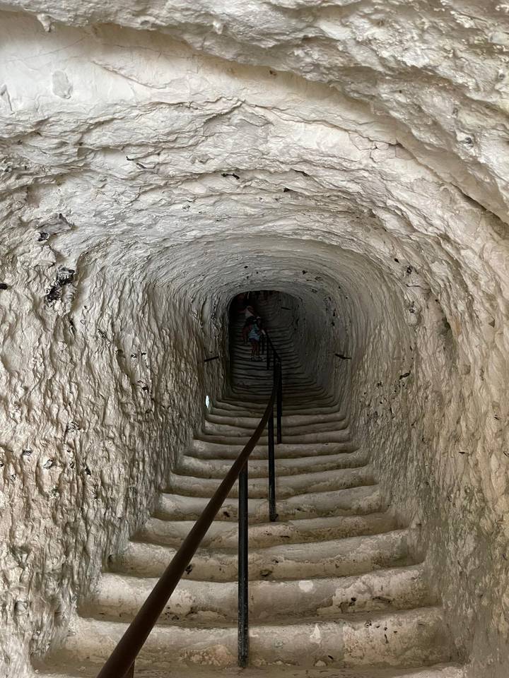 Dimly lit rock tunnel with carved steps descending into the earth with a lone visitor in the distance