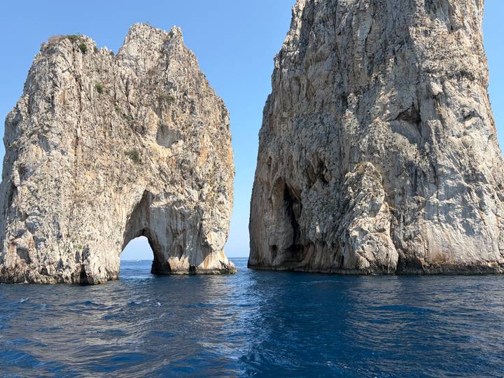Twin towering sea stacks with natural arches rising from deep blue water off the coast of Capri