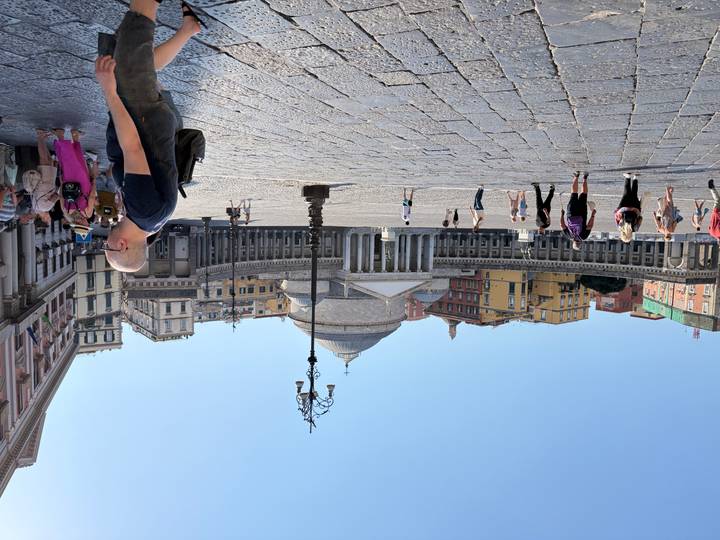 Large open square of Piazza del Plebiscito in Naples with classical dome and columns, visitors strolling
