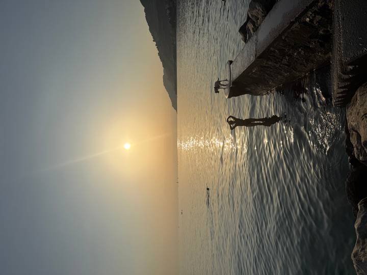 Silhouette of a swimmer and a person with a dog against a golden sunset over a calm lake