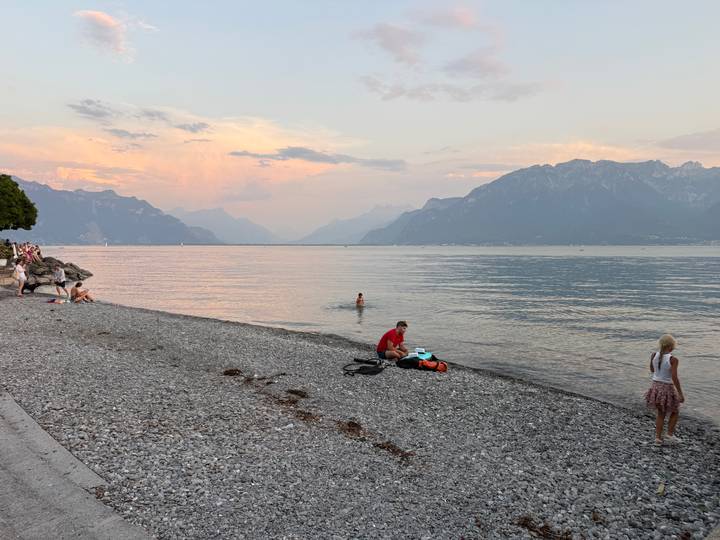 Pebble beach on Lake Geneva at dusk with swimmers and families enjoying the calm water
