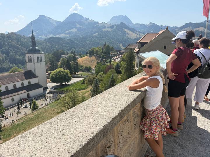 Travelers looking out from Gruyères ramparts toward church steeple and pastoral hills