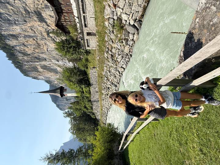 Mother and daughter standing by a fast flowing alpine river with a church spire and cliff backdrop