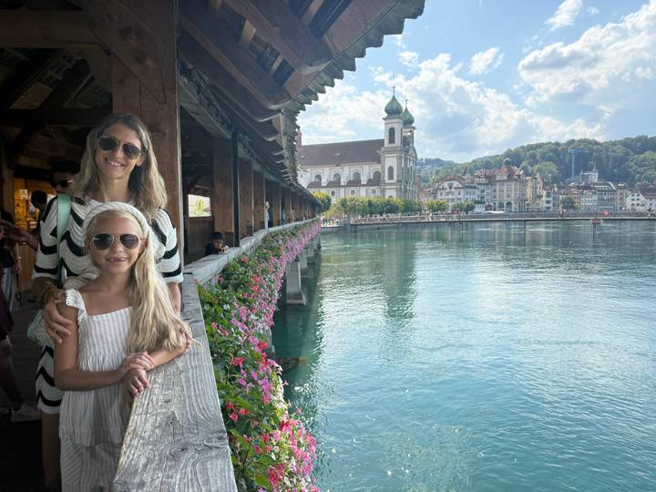 Mother and daughter posing on Lucerne's flower-lined covered bridge with lake and town behind