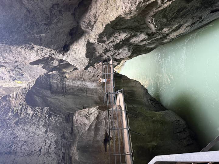 Person standing on a suspended walkway inside a dramatic narrow gorge with turquoise water below