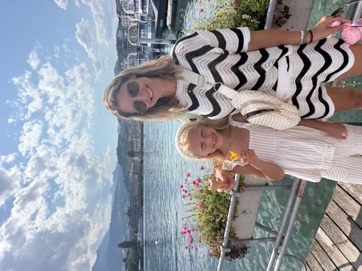 Mother and daughter enjoying ice cream on a lakeside pier with mountains and bright sky