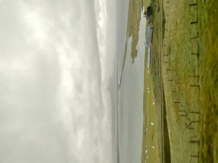 Vertical blurry shot of Icelandic coastline with distant low mountain under grey skies.