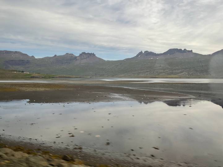 Tidal flats reflecting rugged mountains under overcast skies in East Iceland.