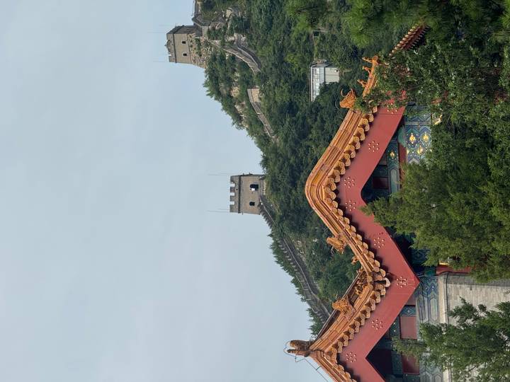 Watchtower of the Great Wall rising above forested ridge with ornate temple roof in foreground.