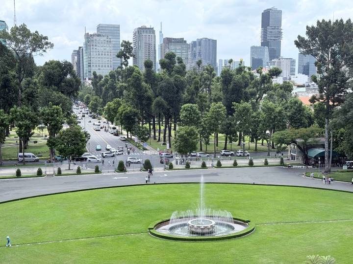 View across manicured lawns and fountain toward a tree-lined boulevard and modern skyline of Ho Chi Minh City.