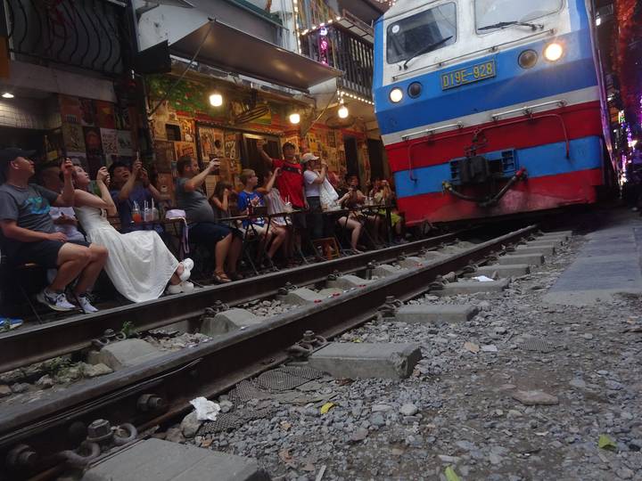 Crowds seated inches from a brightly painted train passing through Hanoi's famous Train Street café alley.