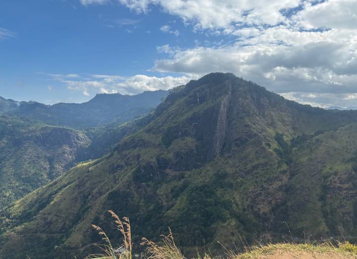 Lush green Sri Lankan mountain ridge under a partly cloudy sky with deep valleys below.