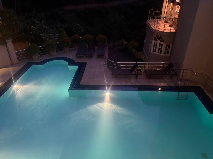 Night view of a hotel swimming pool softly lit with blue underwater lights and loungers nearby.