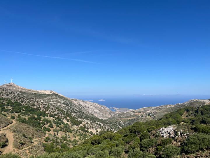Expansive mountain ridge descending to the deep blue Aegean Sea under clear sky.
