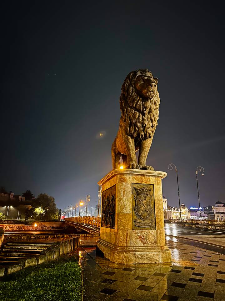 Majestic stone lion statue on pedestal illuminated against dark night sky.