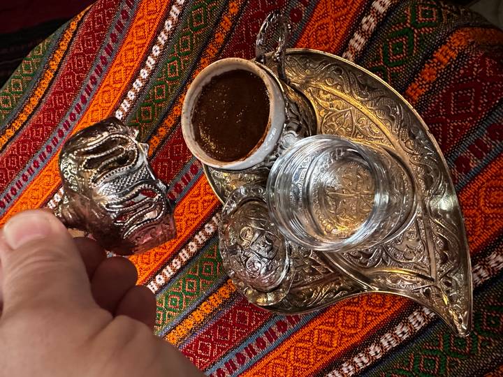 Close-up of traditional Balkan coffee set with ornate metalwork on colourful woven tablecloth.
