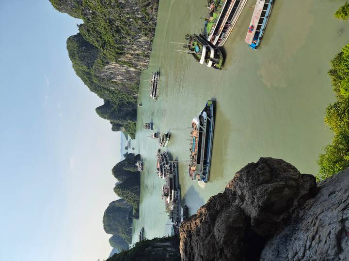 Scenic bay filled with tour boats surrounded by dramatic green limestone cliffs.