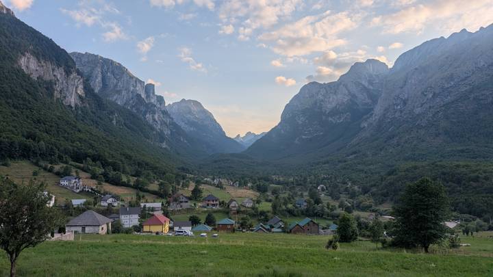 Expansive alpine valley with scattered village houses beneath dramatic jagged peaks at dusk.