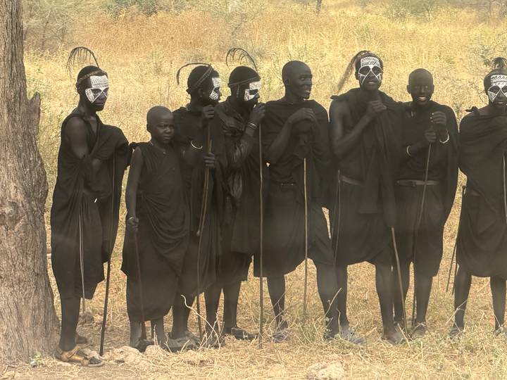 Group of Maasai men in traditional black attire and face paint standing with staffs